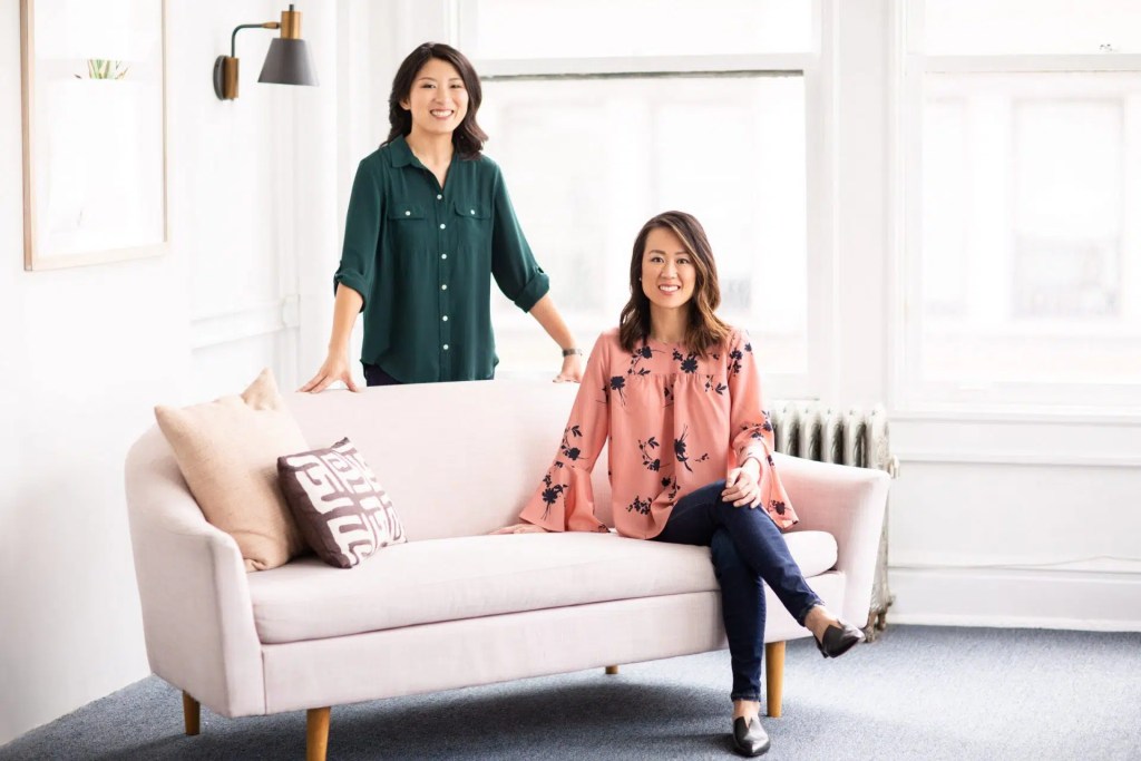A woman standing and a woman sitting on a couch